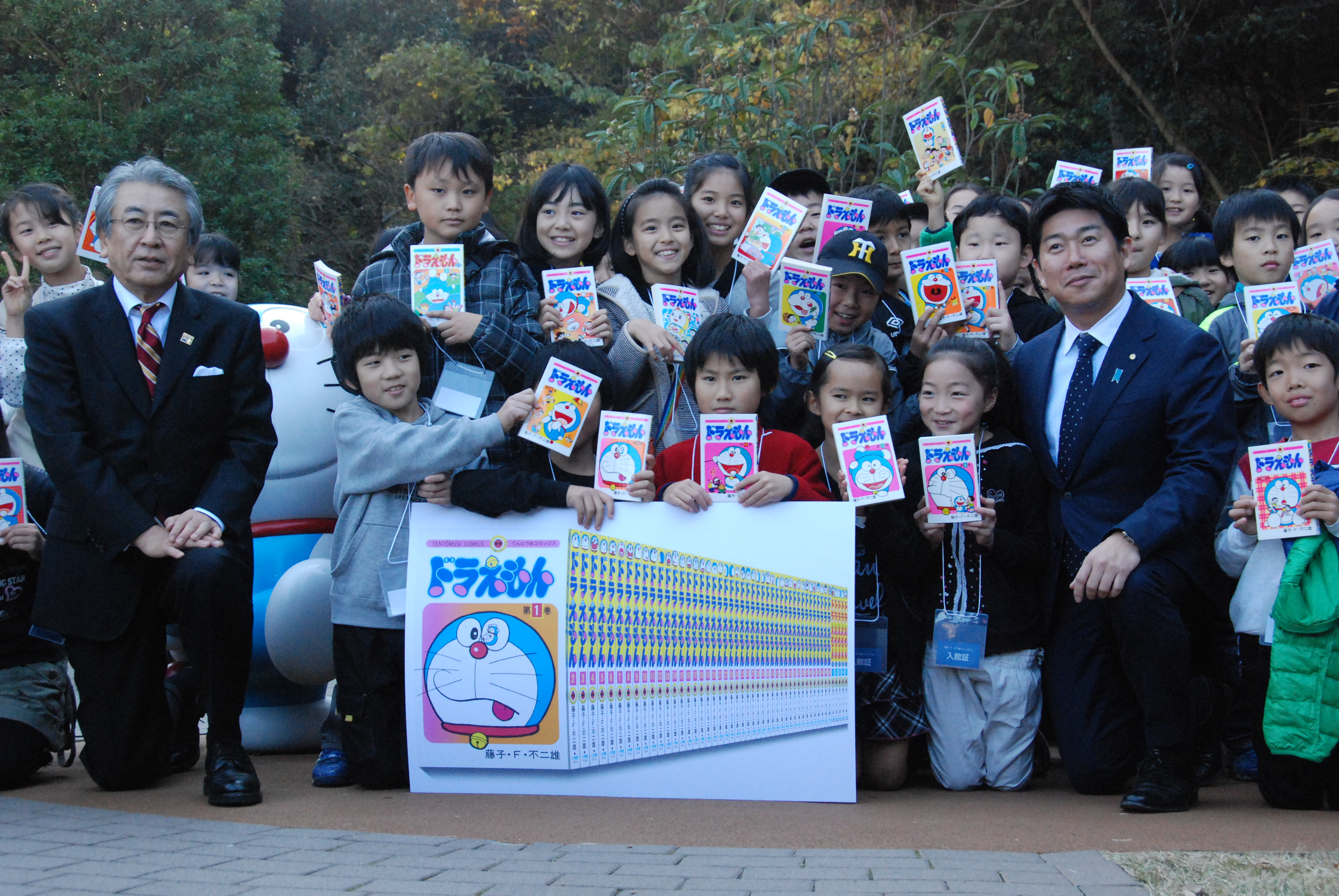 『ドラえもん』の単行本をプレゼントされ喜ぶ子どもたちと、伊藤館長(左)、福田市長(右)