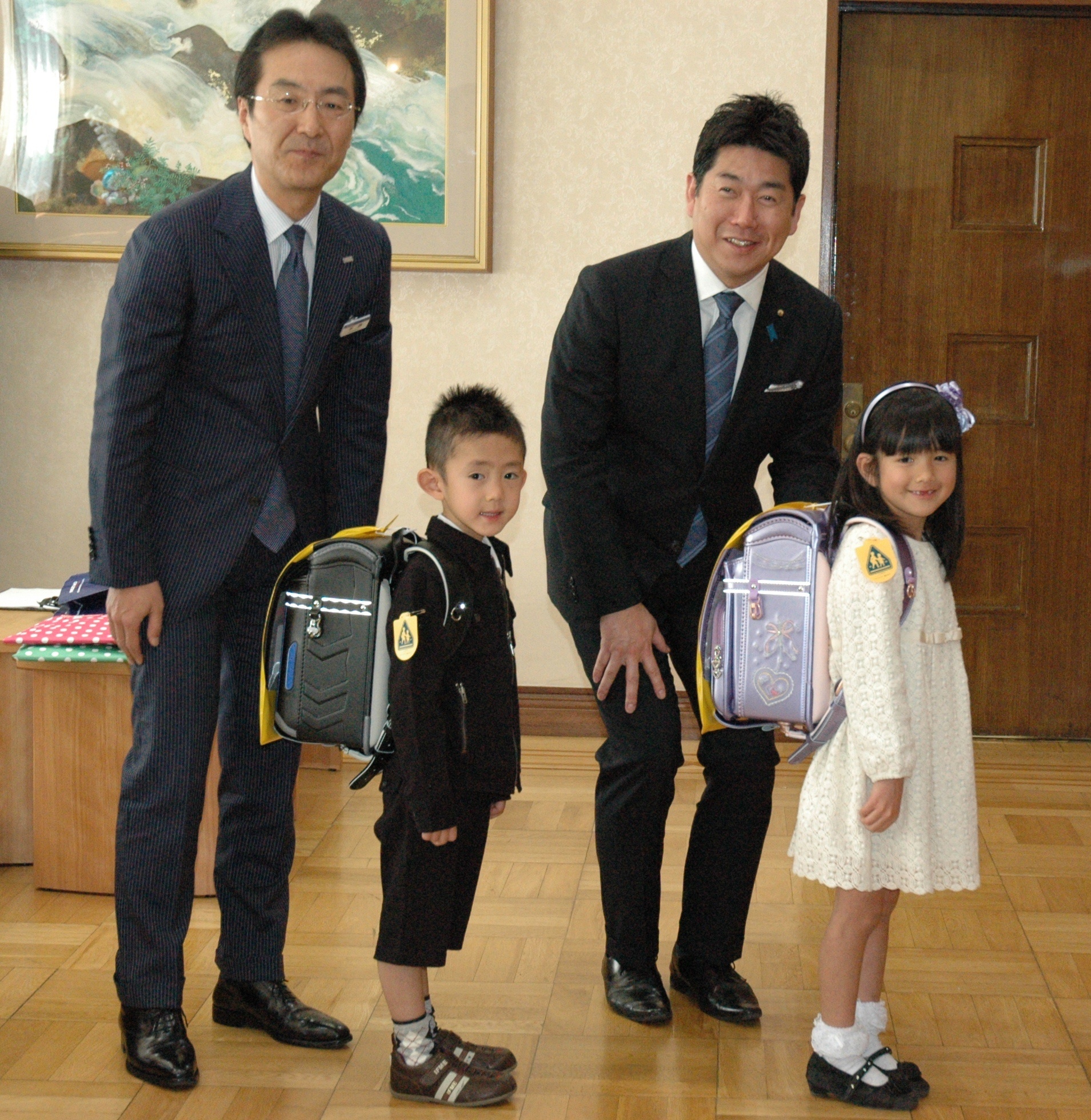 黄色いワッペンを贈られた新入学児童と記念撮影をするみずほ銀行川崎支店の手島隆之支店長(左)と福田市長(右)