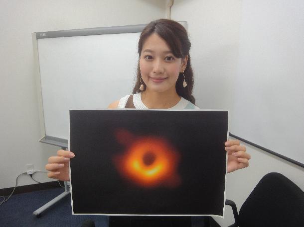 【写真】レポーターがブラックホールの写真を持って写っています