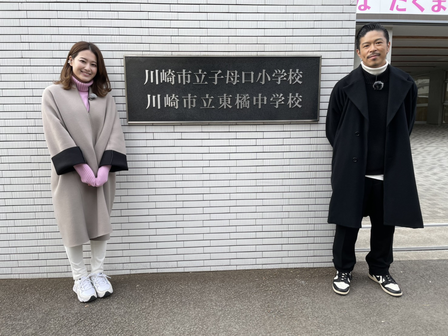 【写真】左プレゼンター、右松本さんが松本さんの母校の前で写っています
