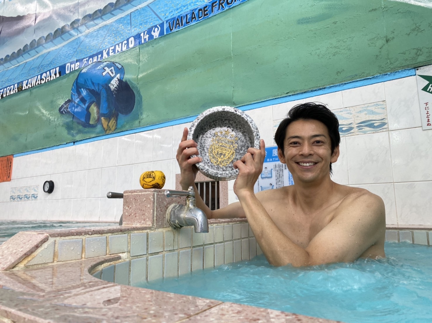 【写真】MC敦士さんがブルーのお湯に浸かって風呂桶を持って写っています