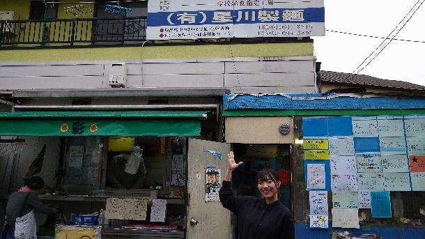 【写真】プレゼンターが定食屋さんの前で写っています