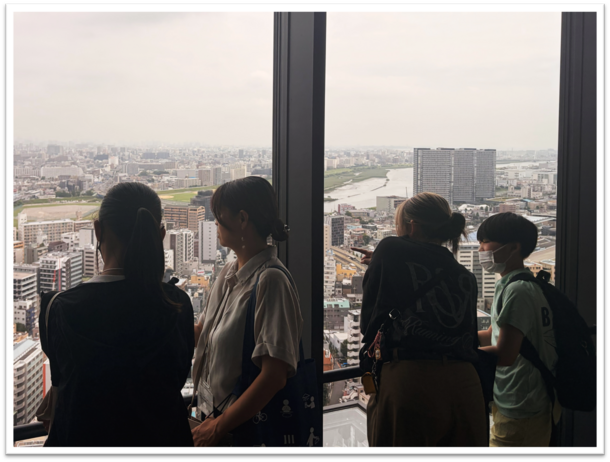 本庁舎25階展望フロアから川崎市の臨海部などの様子を見て、川崎市の大気環境について体感してもらっている様子