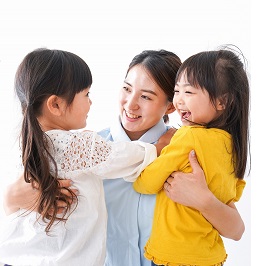 小学生くらいの女の子2人を両腕で抱きしめる女性