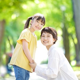 小学生くらいの女の子と正面で両手をつなぎ、笑顔で女の子と一緒に一点を見つめている成人女性