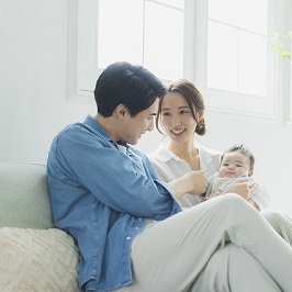 ソファに夫婦が座っており、妻が乳児を抱きかかえている光景