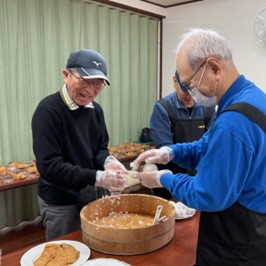 仲間が楽しみながら料理をする地域の集いの写真