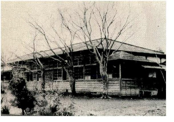 白黒の古い写真。平屋建ての木造の校舎が写っている。