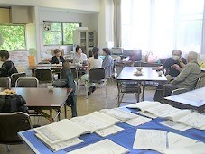 手前に展示された資料、奥に交流カフェで談笑する人々